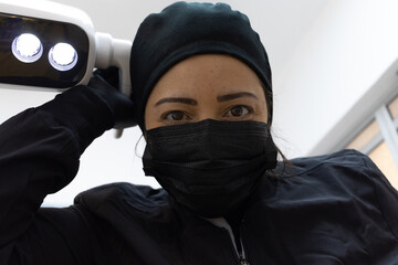 Latin female doctor looking towards camera in working position. Arranging surgical lights. POV.