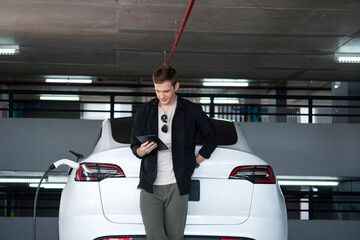 Young man travel with EV electric car to shopping center parking lot charging in downtown city...