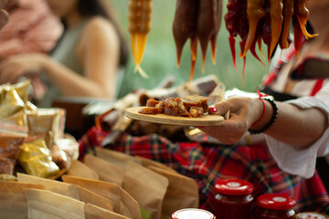 Food tasting. Female hand holds wooden plate and tray with small chopped pieces of meat, sausages, sweets. Woman seller on street fair. Celebrating Tbilisoba holiday. Day of city Tbilisi, Georgia. Eat