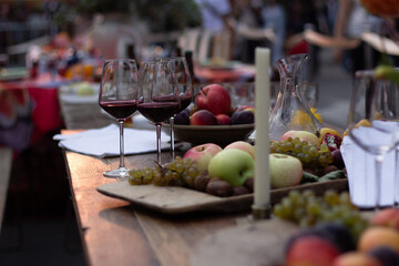 Celebrating Tbilisoba holiday. Day of city Tbilisi, Georgia. Street fair. Table with glass of red wine, grapes, berries, fruits, apples, pomegranate, wax candle. Concept of cooking, dinner, lunch. Eat