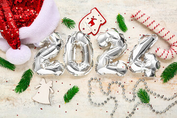 Composition with figure 2024 made of foil balloons, Santa hat and Christmas decorations on light background