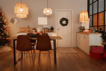 Interior of modern kitchen with glowing lamps, dining table and Christmas tree at evening