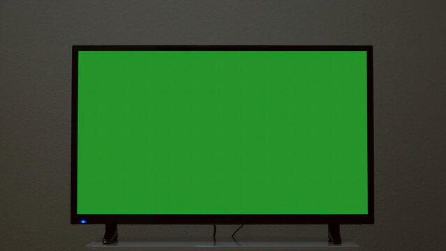 Plasma TV with green screen stands on background wall. Concept. Green-screen TV stands on background gray wall. Green screen TV for inserting chromakey