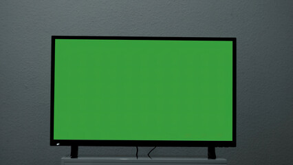 Plasma TV with green screen stands on background wall. Concept. Green-screen TV stands on background gray wall. Green screen TV for inserting chromakey