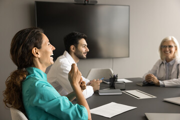 Diverse medical staff having fun on clinic meeting, sitting at large table in boardroom. Cheerful...