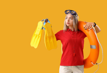 Female lifeguard with ring buoy and flippers on yellow background