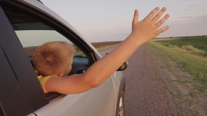 Concept of traveling by car on road. Boy, teenager stretches out his hand from car window, happy...