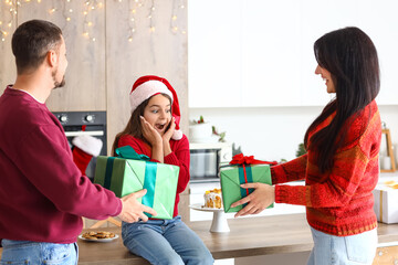 Surprised little girl receiving Christmas presents from her parents in kitchen