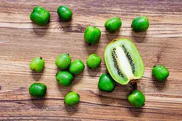 bunch of mini kiwis with one regular kiwi cut in half flat lay on a wooden background