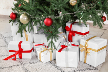 Gift boxes under Christmas tree with balls and glowing lights, closeup