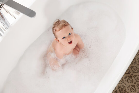 Cute little baby bathing in tub at home, top view