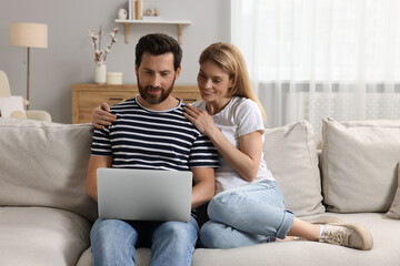 Happy couple with laptop on sofa at home