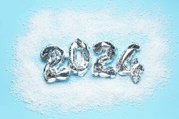 Silver foil balloons number 2024 and snow on blue background. New year concept.