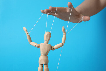 Woman pulling strings of puppet on light blue background, closeup