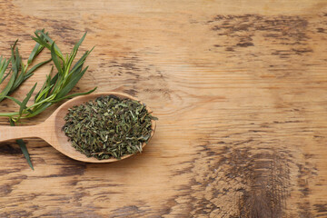 Fototapeta na wymiar Spoon of dry tarragon and green leaves on wooden table, flat lay. Space for text