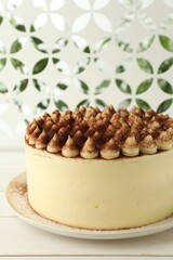 Delicious tiramisu cake with cocoa powder on white wooden table