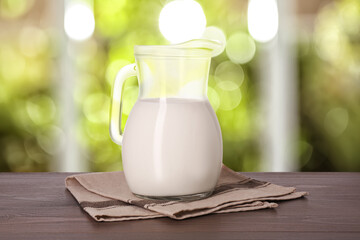 Fresh milk in glass pitcher on wooden table in room
