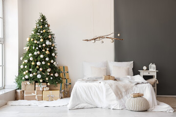 Interior of festive bedroom with comfortable bed, hanging decor and Christmas tree