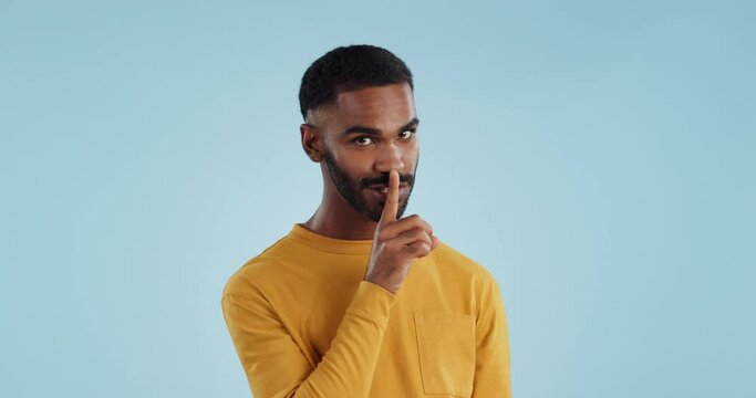 Secret, face and man with finger on lips in studio for quiet, privacy or hush news on blue background. Whisper, drama and portrait of guy model with confidential hand emoji for gossip or announcement