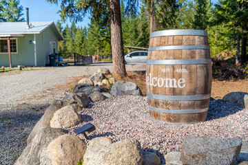 A rustic barrel with the word Welcome stenciled on it as landscaping sits outside the gravel...