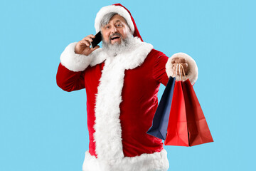 Santa Claus with shopping bags talking by phone on blue background