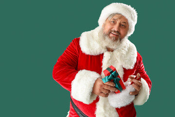 Santa Claus putting present into Christmas sock on green background