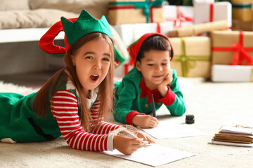 Cute little children dressed as elves writing letters to Santa at home on Christmas eve