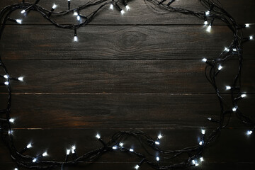 Frame made of beautiful Christmas lights on black wooden background