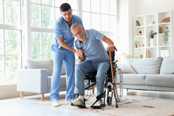 Male nurse helping senior man with stick to stand up at home - obrazy, fototapety, plakaty