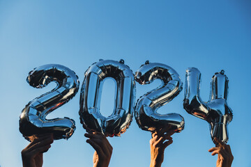 Silver foil number 2024 celebration new year balloon on blue sky background. Happy New year greetings concept. Hands holding balloons two thousand twenty-fourth year Christmas holiday concept 