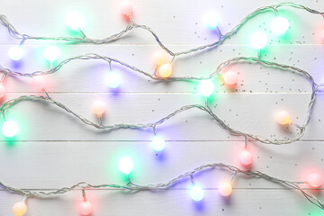 Glowing Christmas lights on white wooden background