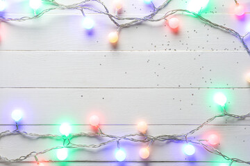 Frame made of glowing Christmas lights on white wooden background