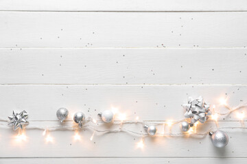Glowing Christmas lights with balls on white wooden background