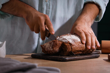 Young man cutting fresh bread at table in bakery
