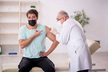 Obraz premium Young male patient visiting old male doctor in vaccination conce