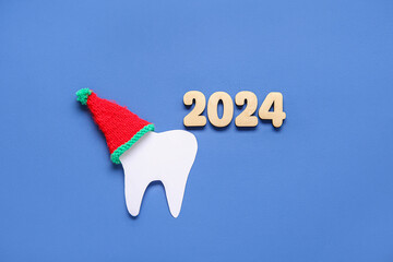 Figure 2024 and paper tooth with Santa hat on blue background
