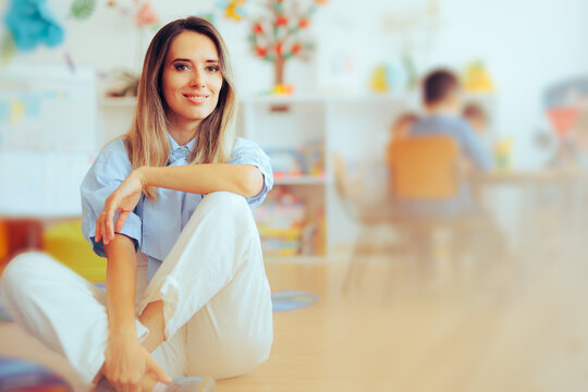 Kindergarten Teacher Sitting On The Floor Smiling Friendly. Relaxed Teacher Practicing Her Profession With A Positive Attitude 
