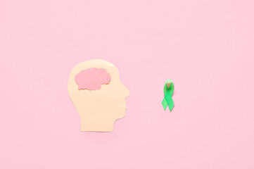 Paper human head with brain and green awareness ribbon on pink background. Mental Health Day