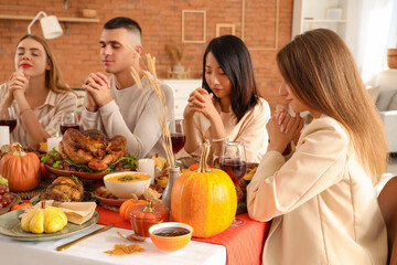 Group of young friends praying before dinner at festive table on Thanksgiving Day