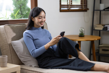 Obraz premium Portrait of Happy casual beautiful asian woman accountant is sitting using a phone on sofa and relaxing on her mobile application at home.