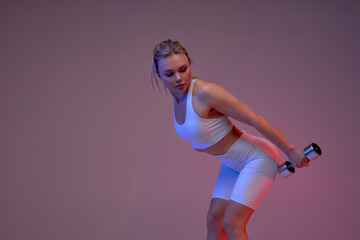 awesome sporty girl bending her back toward, looking back at dumbbells. close up portrait, isolated purple background. copy space