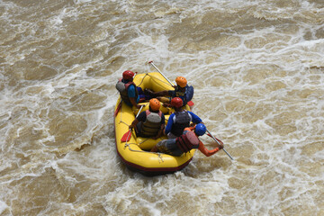 A group of tourists guided by a professional pilot on white water rafting, on a murky river after...