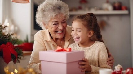 Fototapeta na wymiar Grandmother congratulates child with gift box. Kid and senior woman are hugging in cozy home kitchen. Family enjoying kindness, tenderness. Lifestyle moment. Happy holidays Christmas, Birthday