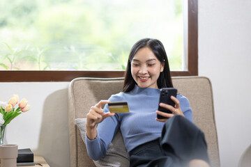 Young asian woman holding credit card and shopping or online payment by using nusing phone laptop computer. Businesswoman at home. Online shopping, e-commerce, internet banking, spending money.