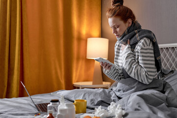 A sick woman is holding a sore throat using a phone in her hand. woman sitting on home bed in bedroom close up side view portrait, girl looking for information how to treat herself, making phone call - obrazy, fototapety, plakaty