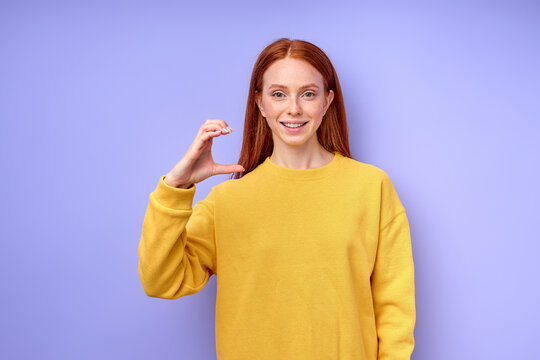 Young smiling red-haired deaf woman wearing yellow sweater using sign language on blue background, girl teaching deaf children to alphabet, education close up portrait, female shows letter C