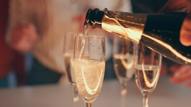 Bartender hand pouring champagne glasses at terrace closeup. Friends toasting