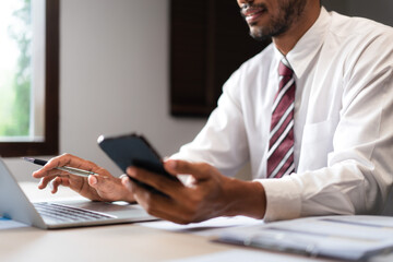 Businessman researching data on smartphone and typing on laptop while analyzing strategy of startup