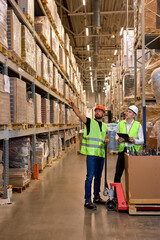 Caucasian warehouse managers walking through large warehouse distribution center discussing about...