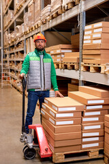 caucasian warehouse worker with manual pallet jack, working in storage room, transporting cardboard goods, boxes delivery. logistics and distribution concept. man in uniform look at camera